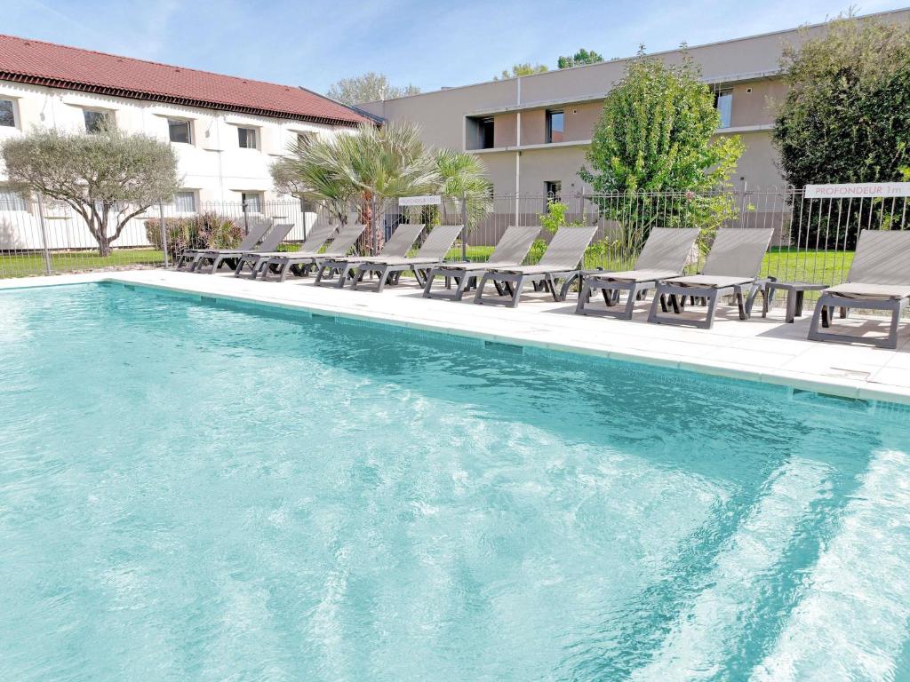 a swimming pool with chaises and chairs next to a building at ibis Aix en Provence in Aix-en-Provence