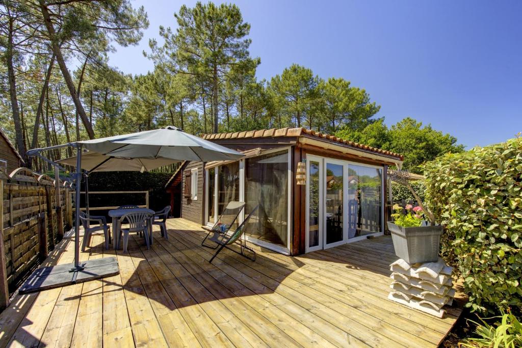 a wooden deck with an umbrella and a house at Comfortable chalet in a vacation village in Gujan-Mestras