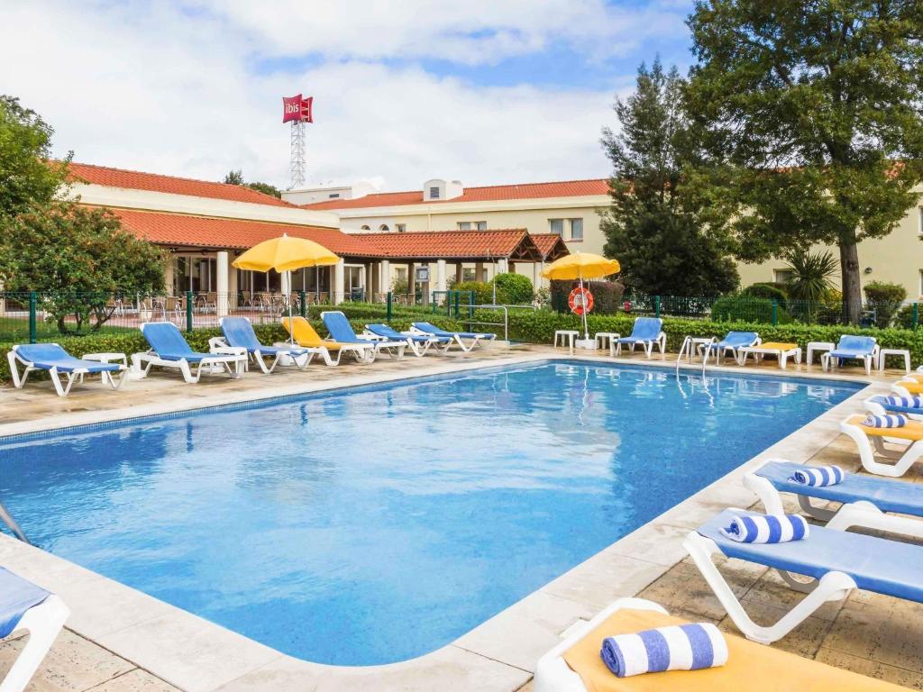 a pool with chairs and umbrellas in front of a hotel at Hotel ibis Setubal in Setúbal