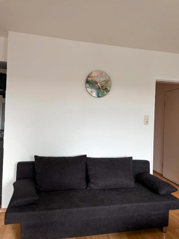 a black couch against a white wall with a clock at Mocafe Schloßbleiche in Wuppertal