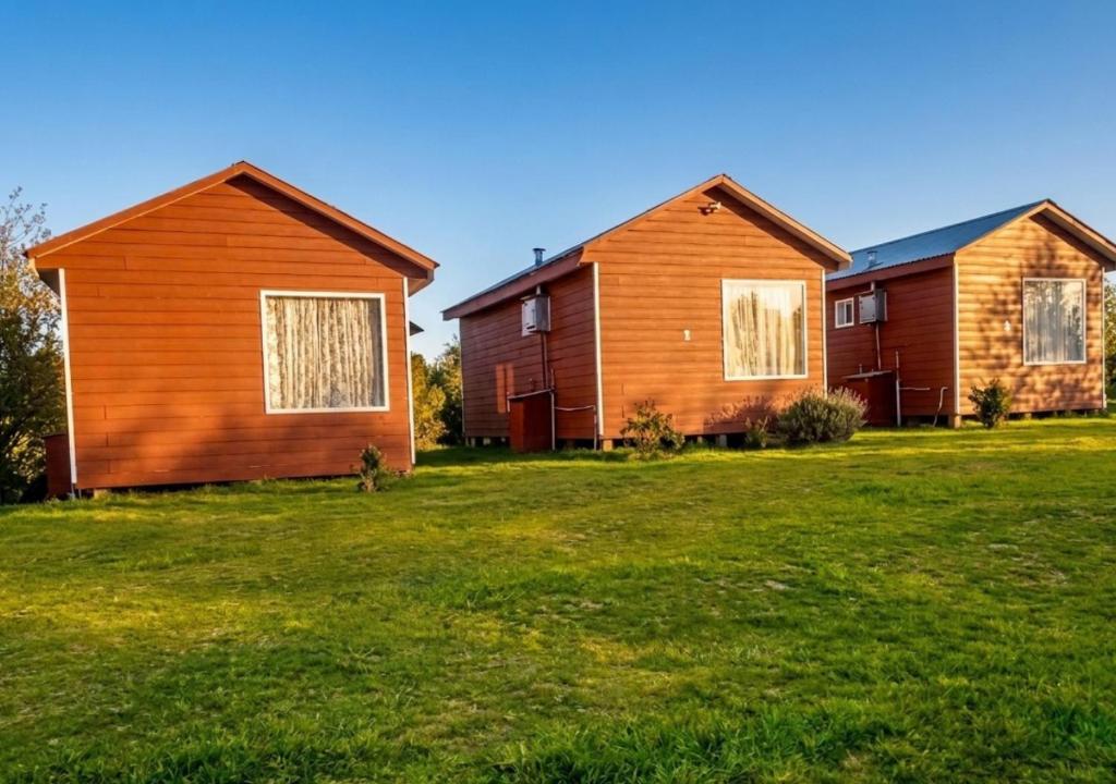 a group of three houses in a grass field at Refugio Pradera del Sur in Llanquihue
