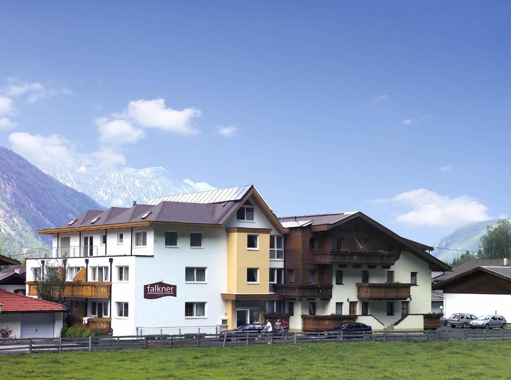 a building in a field with mountains in the background at Falkner Appartement Resort in Längenfeld
