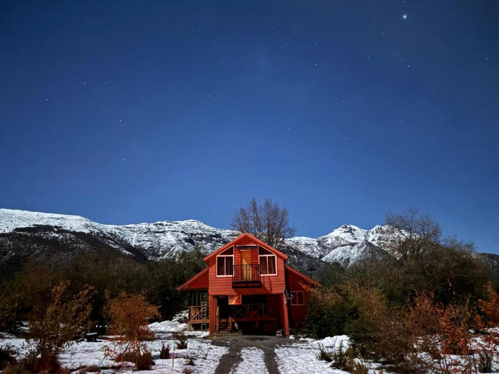 a red cabin in the snow with snow covered mountains at Cabaña Laguna Huemul in Pinto