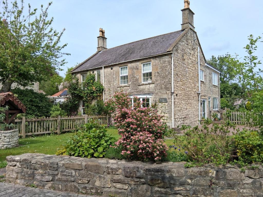 an old stone house with a stone fence and flowers at Crooked Well in Bath