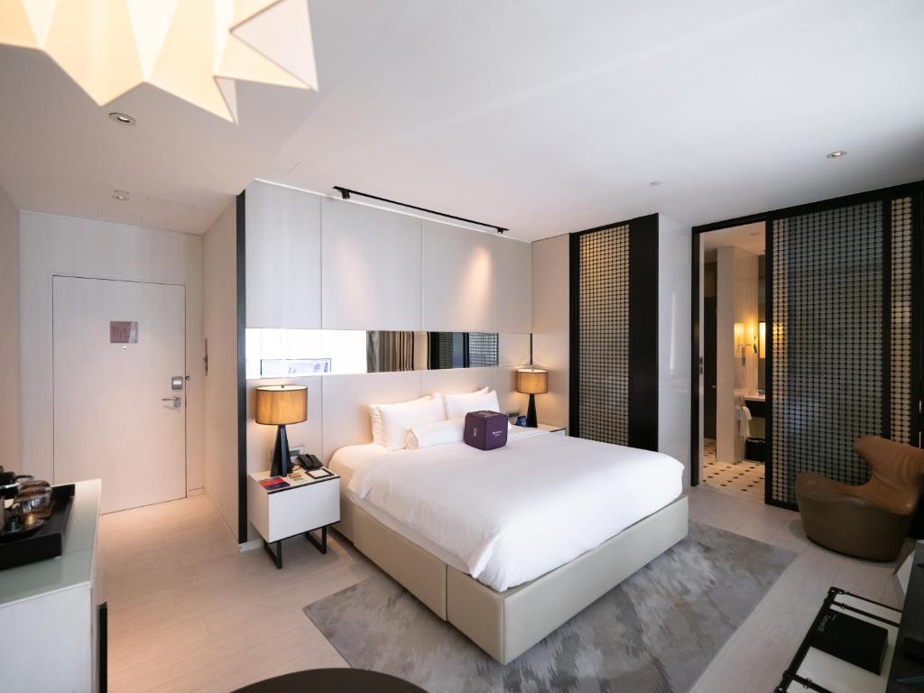a bedroom with a white bed and a living room at Naumi Hotel Singapore in Singapore