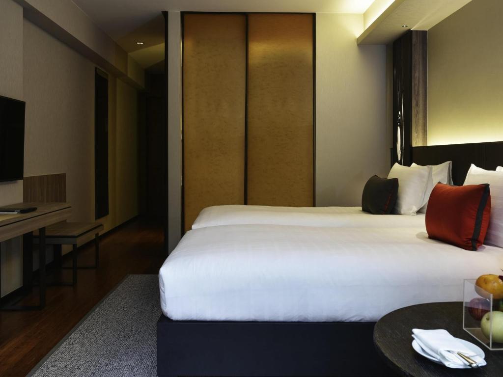 A warmly lit guest room with a large bed, bedside table, television, and full-height storage panels.