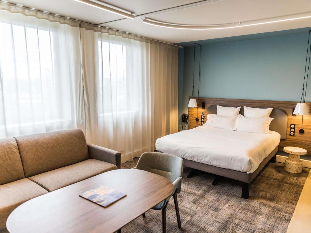 a hotel room with a bed and a couch at Novotel Suites Rouen Normandie in Rouen