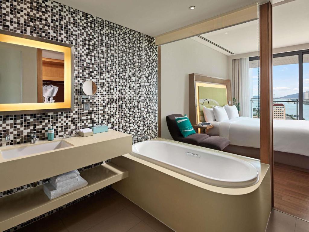 A bright bathroom with a freestanding-style tub beside a bedroom and city view.