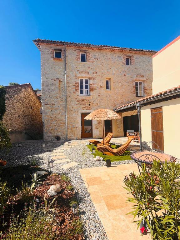 a building with a patio with chairs and an umbrella at Maison Laroque & Spa in Bellefont-La Rauze