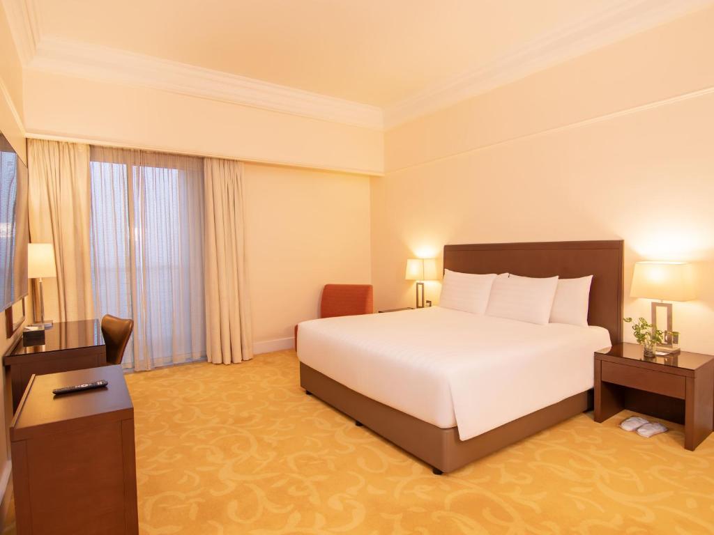 A bedroom with a large bed, writing desk and fully curtained window.