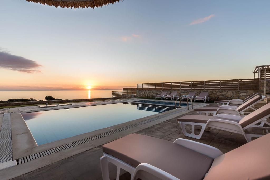 a swimming pool with white chairs and the sunset at Villa Lefkopetra in Triopetra
