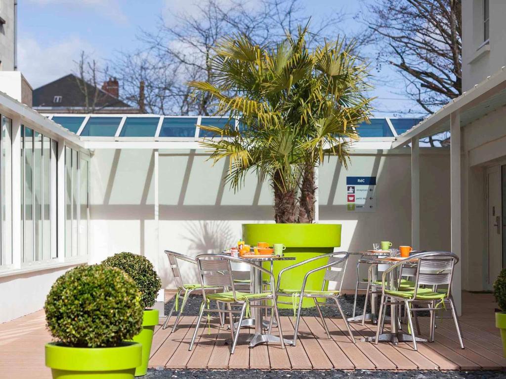 a patio with chairs and a table and a palm tree at ibis Styles Saumur Gare Centre in Saumur