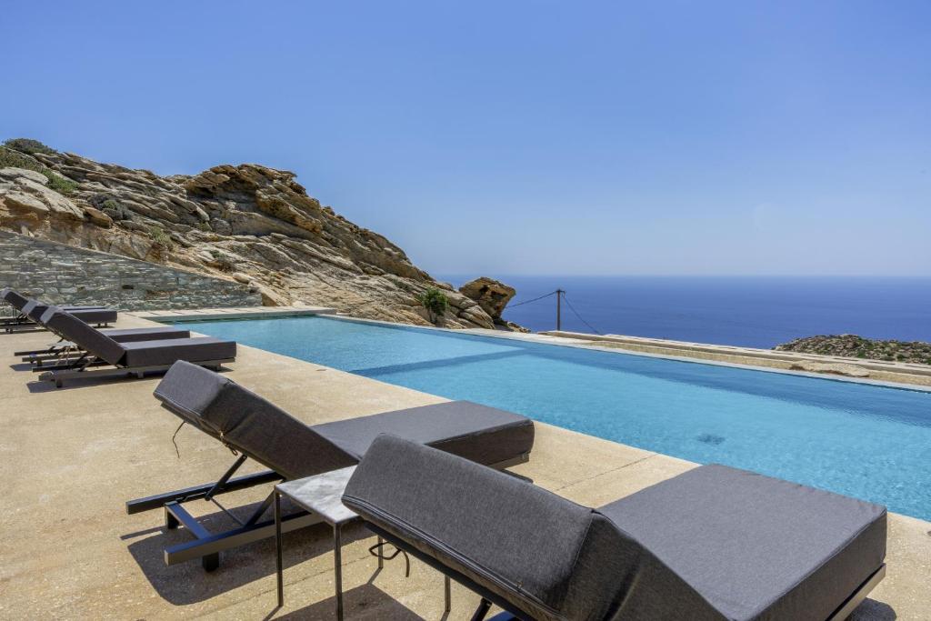 a swimming pool with chairs and the ocean in the background at Aetos Cave Villa With Sunset in Mylopotas