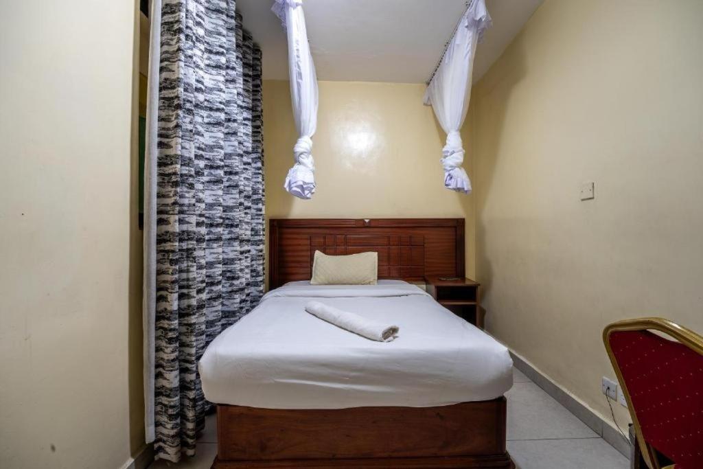 a small bedroom with a bed with white sheets at Capital comfort Hotel Ambala Rd in Nairobi