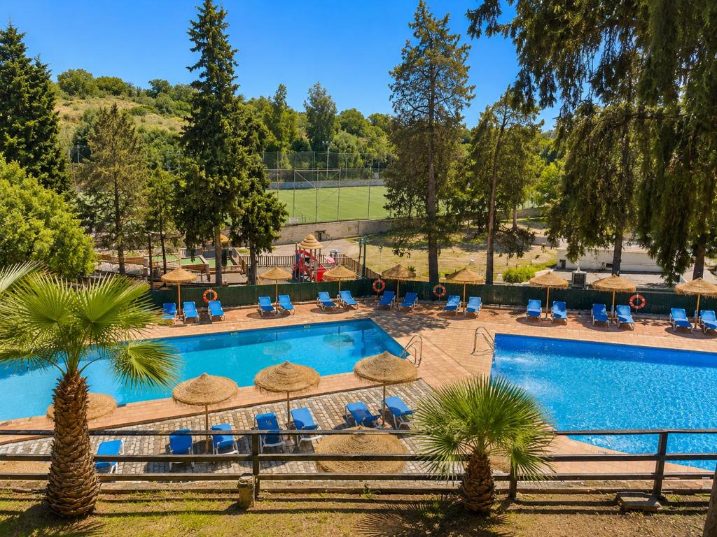 a resort pool with chairs and umbrellas and trees at DWO Finca Los Abetos in Córdoba