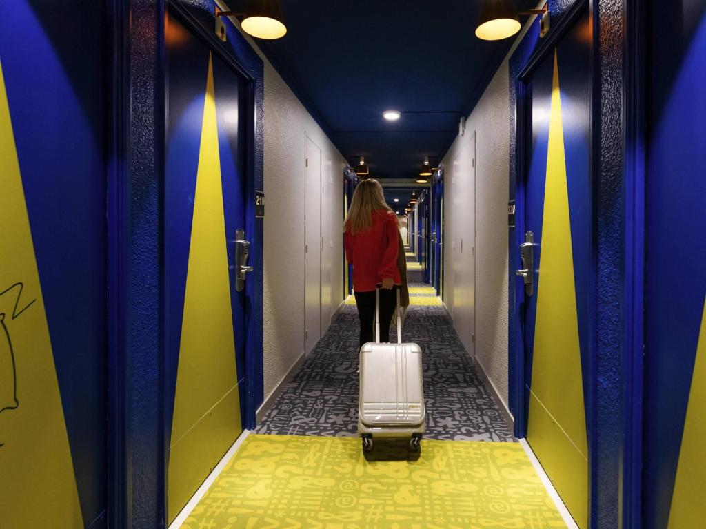 a woman walking down a hallway with a suitcase at ibis budget Albertville in Gilly-sur-Isère