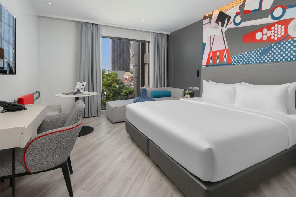 A spacious-looking bedroom with a large bed, desk and window-side sofa.