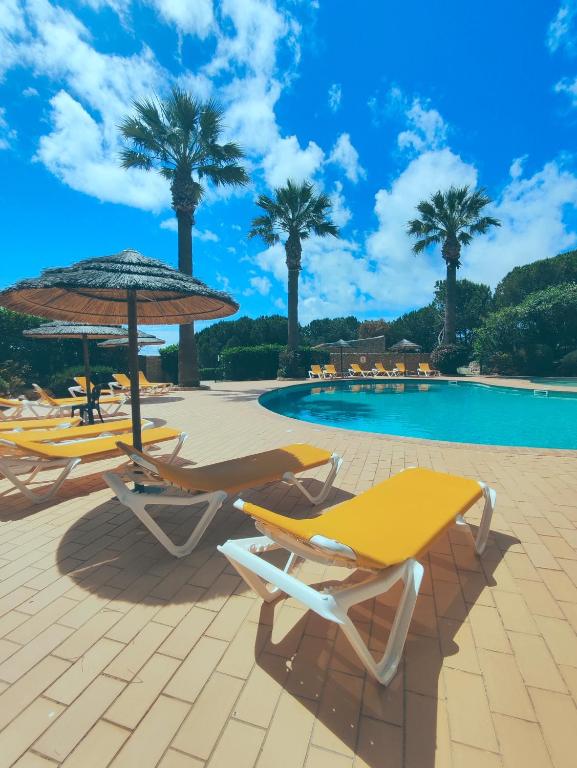 a group of chairs and umbrellas next to a pool at Villa Sunrise by MOJE Holiday in Budens