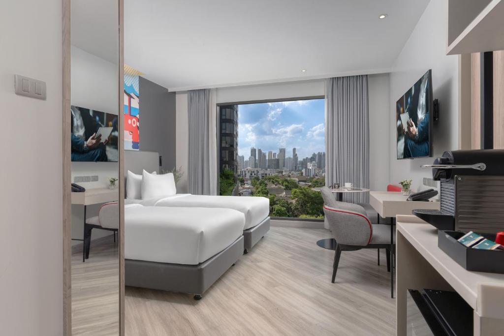 A bedroom with a desk, television, lounge chair and broad city view.