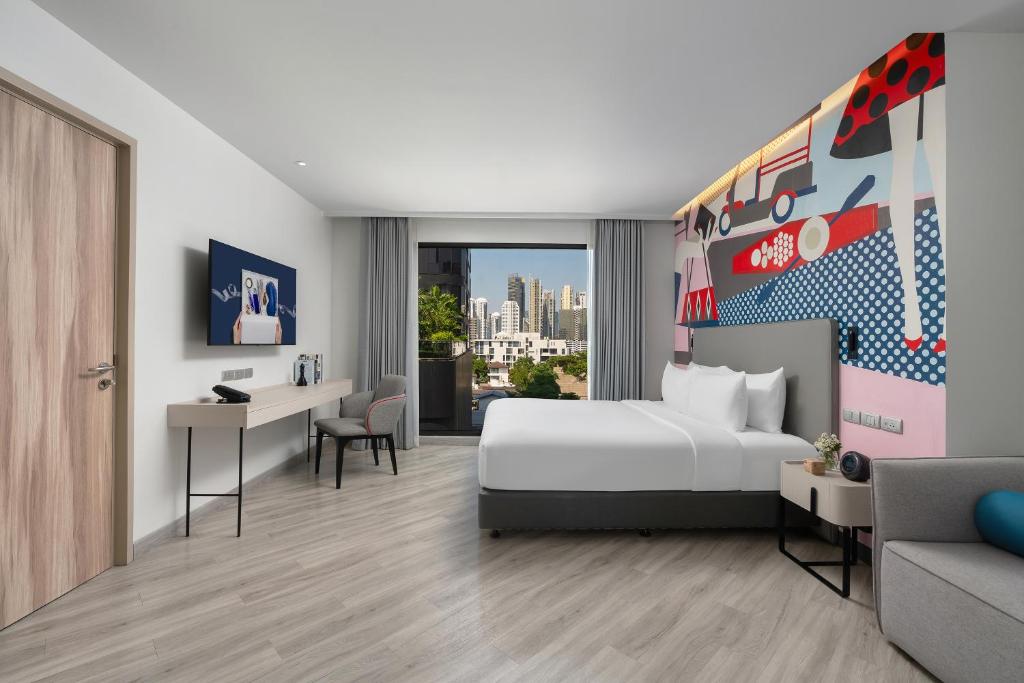 A bright studio-style room with a bed, desk, sofa and city outlook.