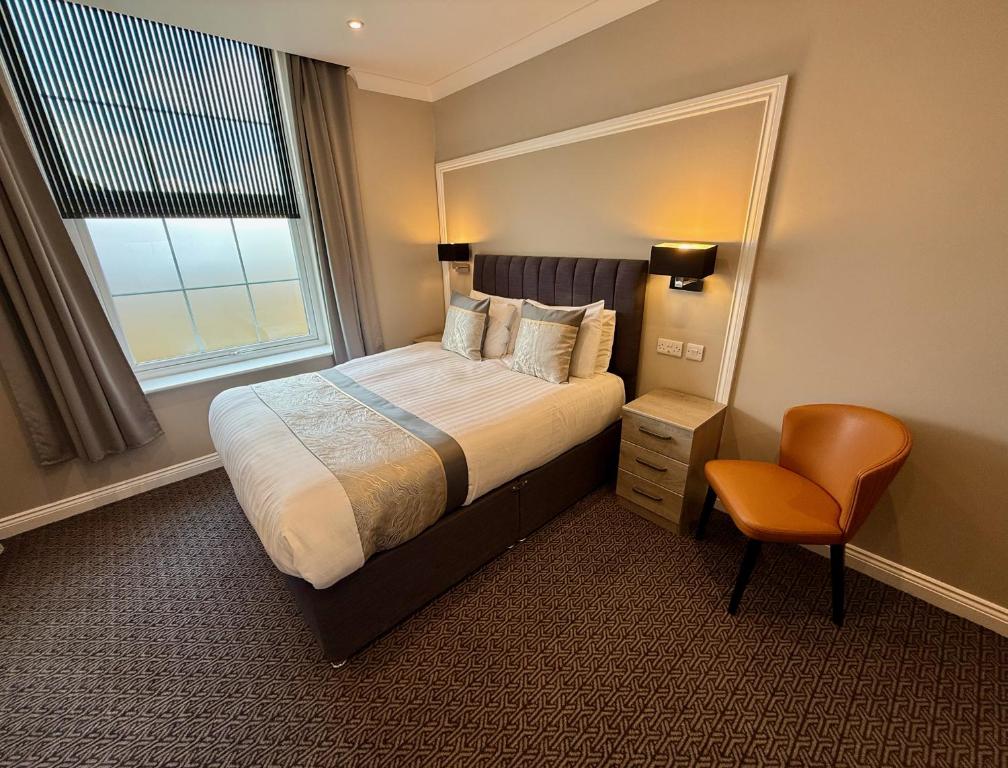 a hotel room with a bed and a chair and a window at The Raven Hotel in Corby