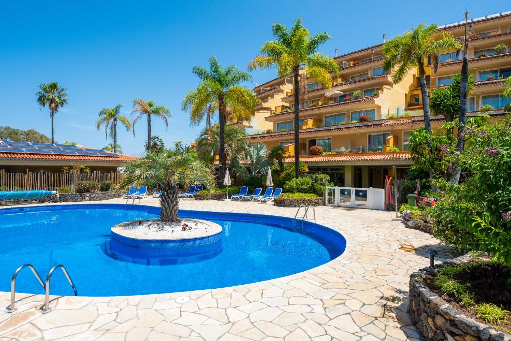 a resort pool with palm trees and a building at Apartamentos Tigaiga Suites in Puerto de la Cruz