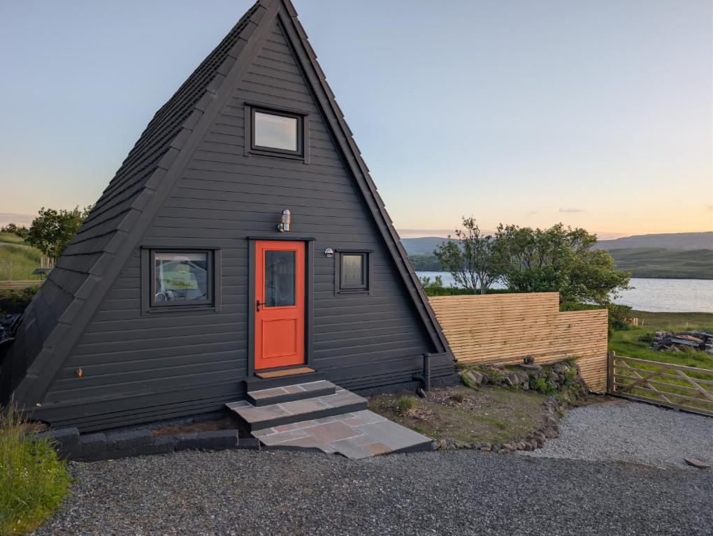 a black house with a red door and a fence at The Chalet, Kildonan in Edinbain