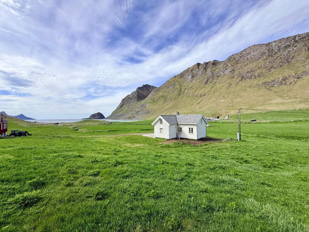 a small white house in a field with mountains at The Haukland House, Between Peaks & Sea in Leknes