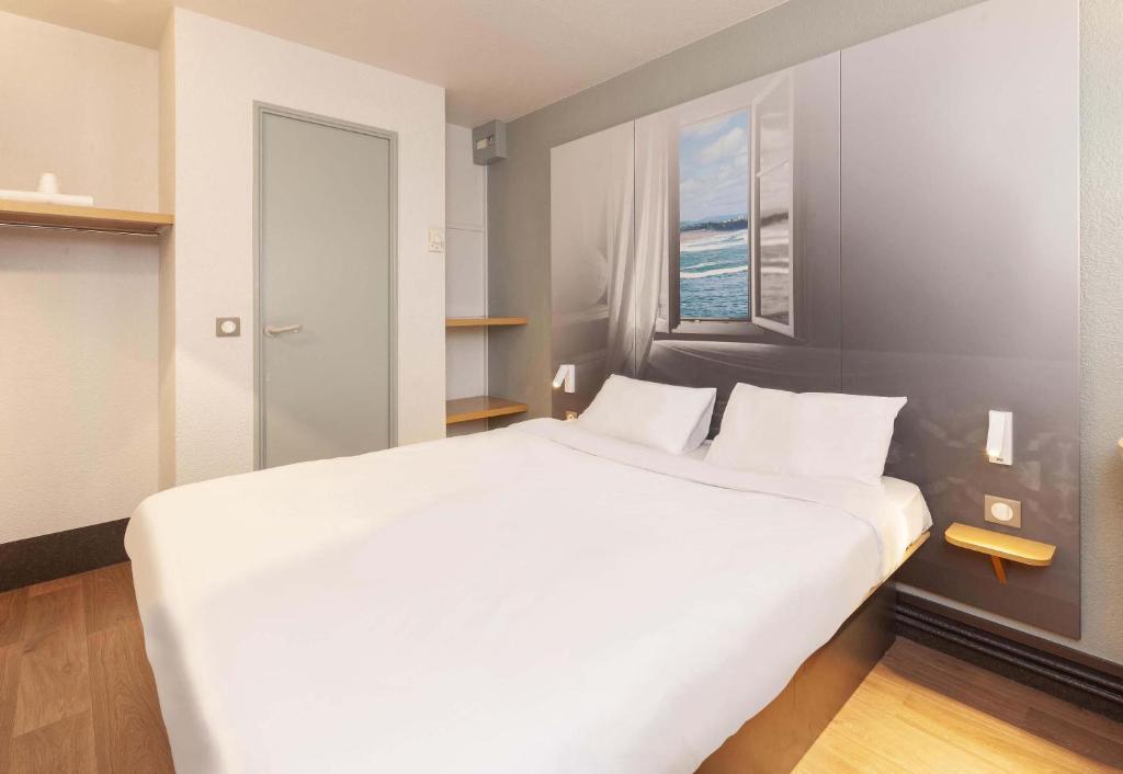 a large white bed in a room with a window at B&B HOTEL Bayonne in Bayonne