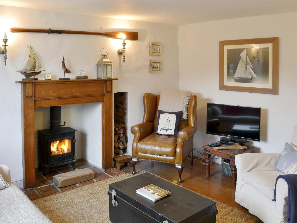 a living room with a fireplace and a chair and a tv at Sea Breeze in Blakeney
