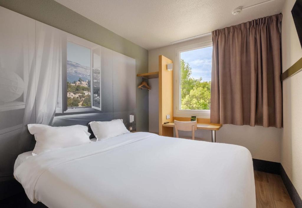 a bedroom with a large white bed and two windows at B&B HOTEL Antibes Sophia Antipolis in Biot