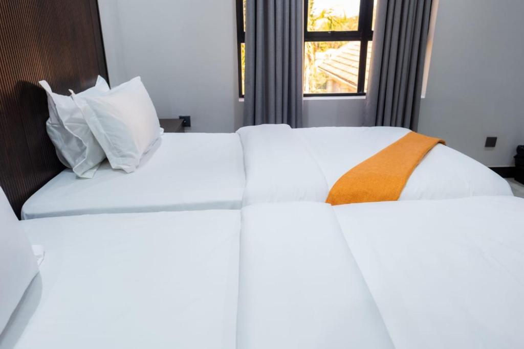 a bed with white sheets and an orange blanket at Purpose International Hotel Eastlea in Harare