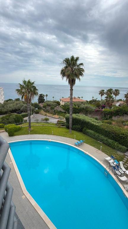 a large blue swimming pool with palm trees and the ocean at Taormina Belu Beach Apartment in Letojanni