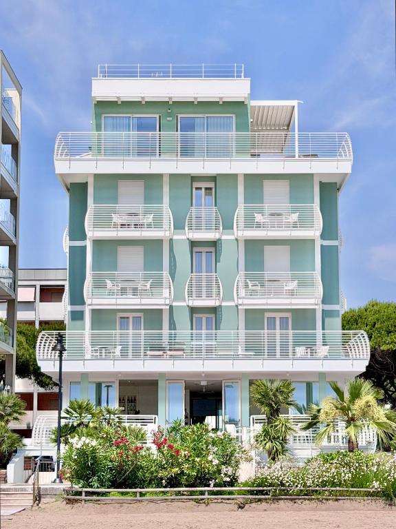 a green building with white balconies and palm trees at Hotel Royal Garnì in Caorle