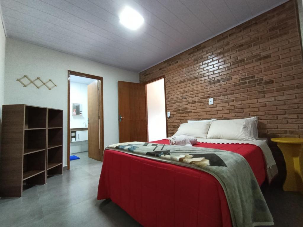 a bedroom with a red bed and a brick wall at Kitnet Sol e Lua in Caparaó Velho