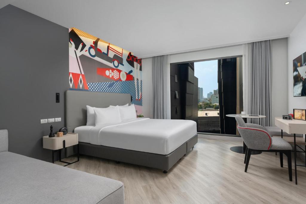 A modern bedroom with a king bed, desk and chair facing a city view.