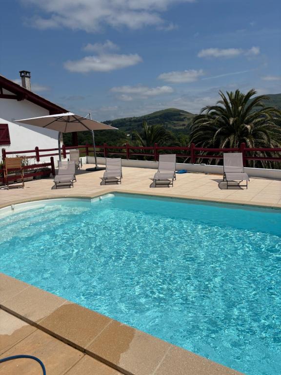 a swimming pool with chairs and an umbrella at L'Estel in Hasparren