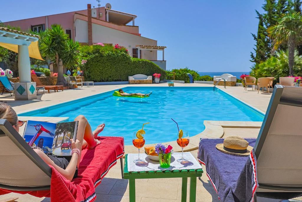a woman sitting on a chair in front of a swimming pool at Passione Mare in Porto Palo