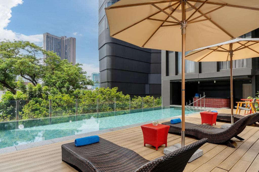 Poolside loungers and umbrellas line a wooden deck beside a glass-edged swimming pool.