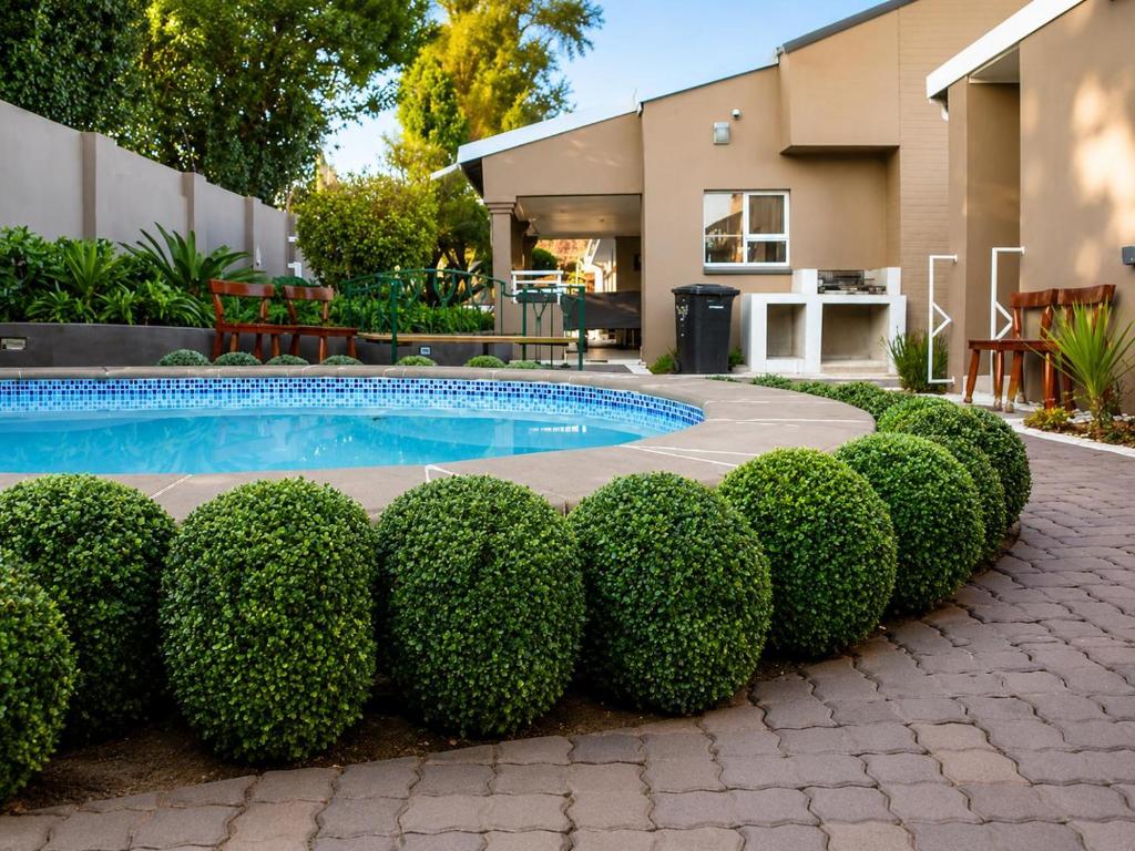 a row of bushes next to a swimming pool at Comfort e Casa Lodge Near OR Tambo Airport in Kempton Park