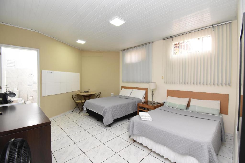a hotel room with two beds and a desk at Loft Jardim Botânico 2 in Curitiba