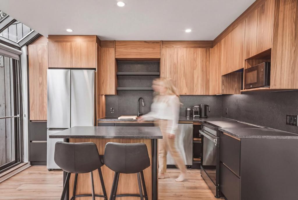 a woman walking through a kitchen with wooden cabinets at 206 Val-des-Neiges - MSA LUX in Beaupré