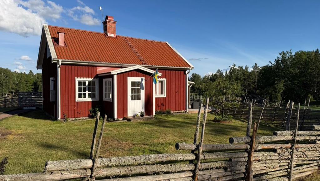 a red house in a field with a fence at Mysigt torp på bondgård in Lämmedal