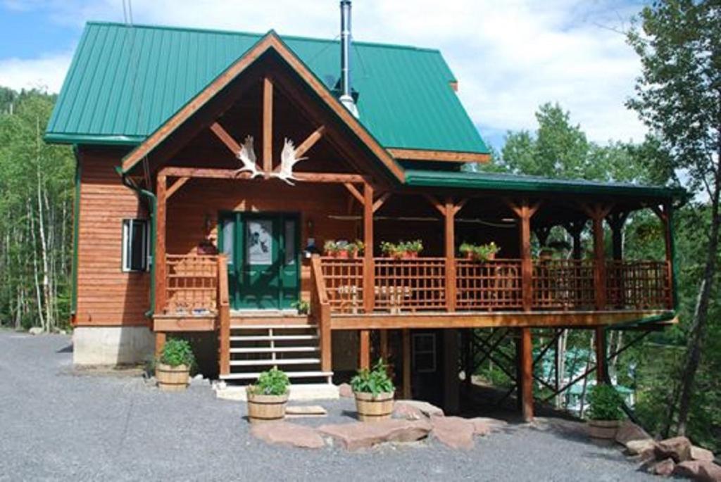 Cabaña de madera con techo verde y porche en Auberge de la Rivière Matapédia - Matapédia River Lodge, en Routhierville