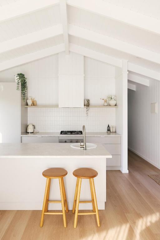 a white kitchen with two stools and a sink at Drift, Port Campbell in Port Campbell