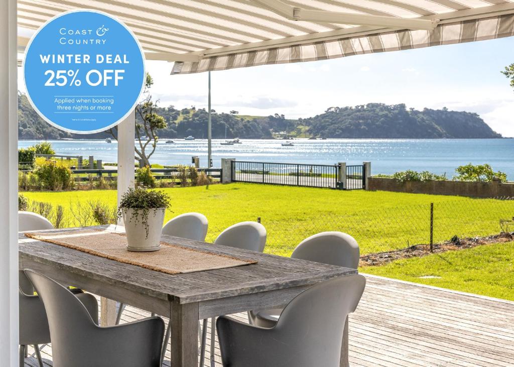 a table with white chairs and a view of the ocean at Bach on the Beach - Coast & Country in Onetangi