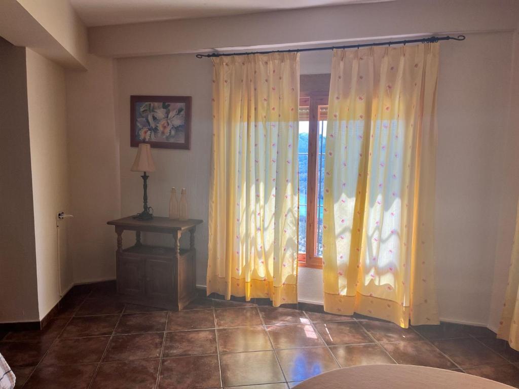 a room with yellow curtains and a table and a window at Apartamentos Esencia vistas al embalse 2 in Hornos