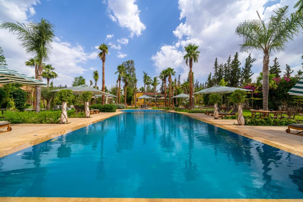 a large blue swimming pool with palm trees and umbrellas at Jnane Rihane Marrakech in Marrakesh