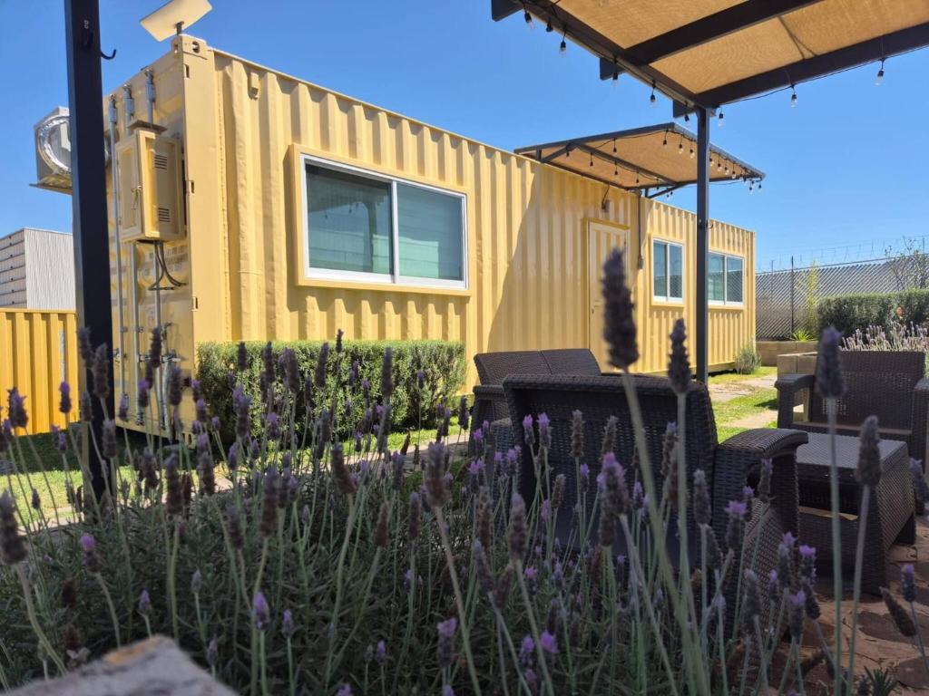 a yellow tiny house in a garden with purple flowers at Container Glamping in Zapopan