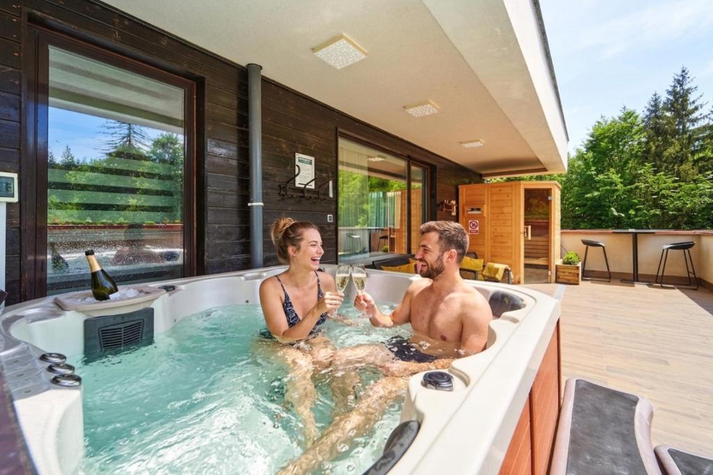 a man and woman sitting in a bath tub with glasses of wine at Mariah Spa Deluxe Adults Only in Poiana Brasov